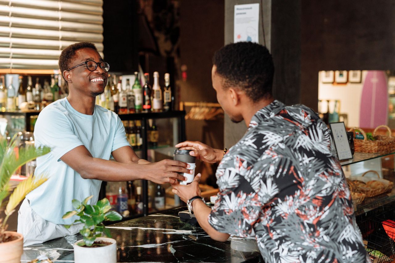A shopkeeper handing a drink directly to a customer over the counter